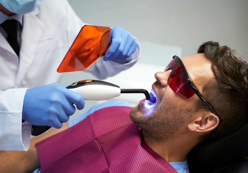 Young man in glasses sitting in dental chair with his mouth open while receiving laser treatment