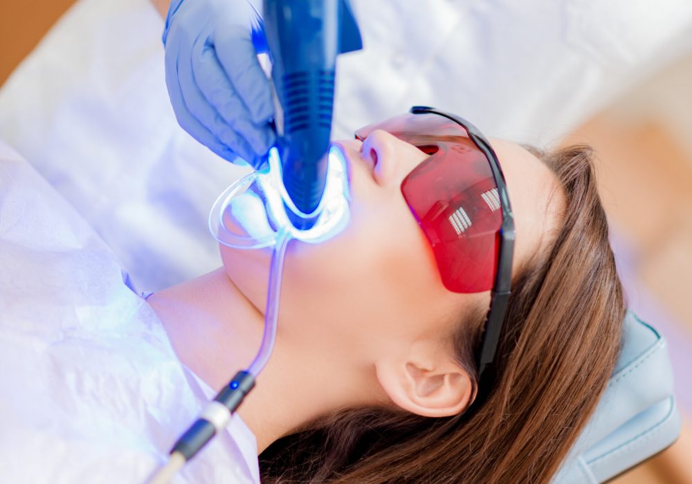 Beautiful young woman in visit at the dentist office. She is whitening teeth with ultraviolet light.